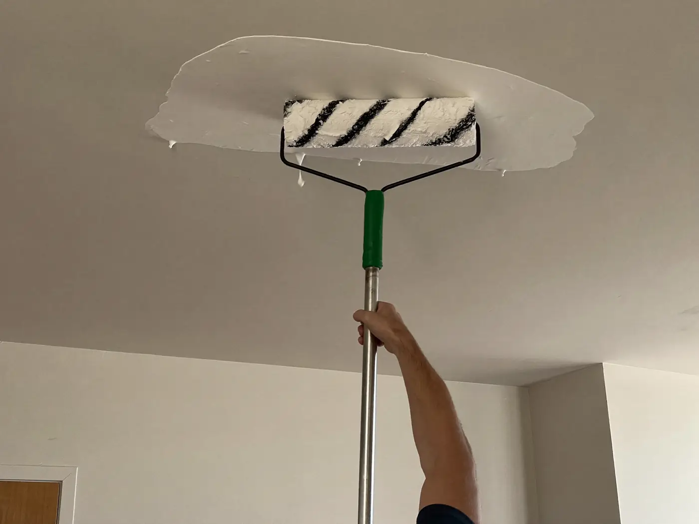 Pintor pintando el techo con rodillo de pértiga en un piso de Terrassa