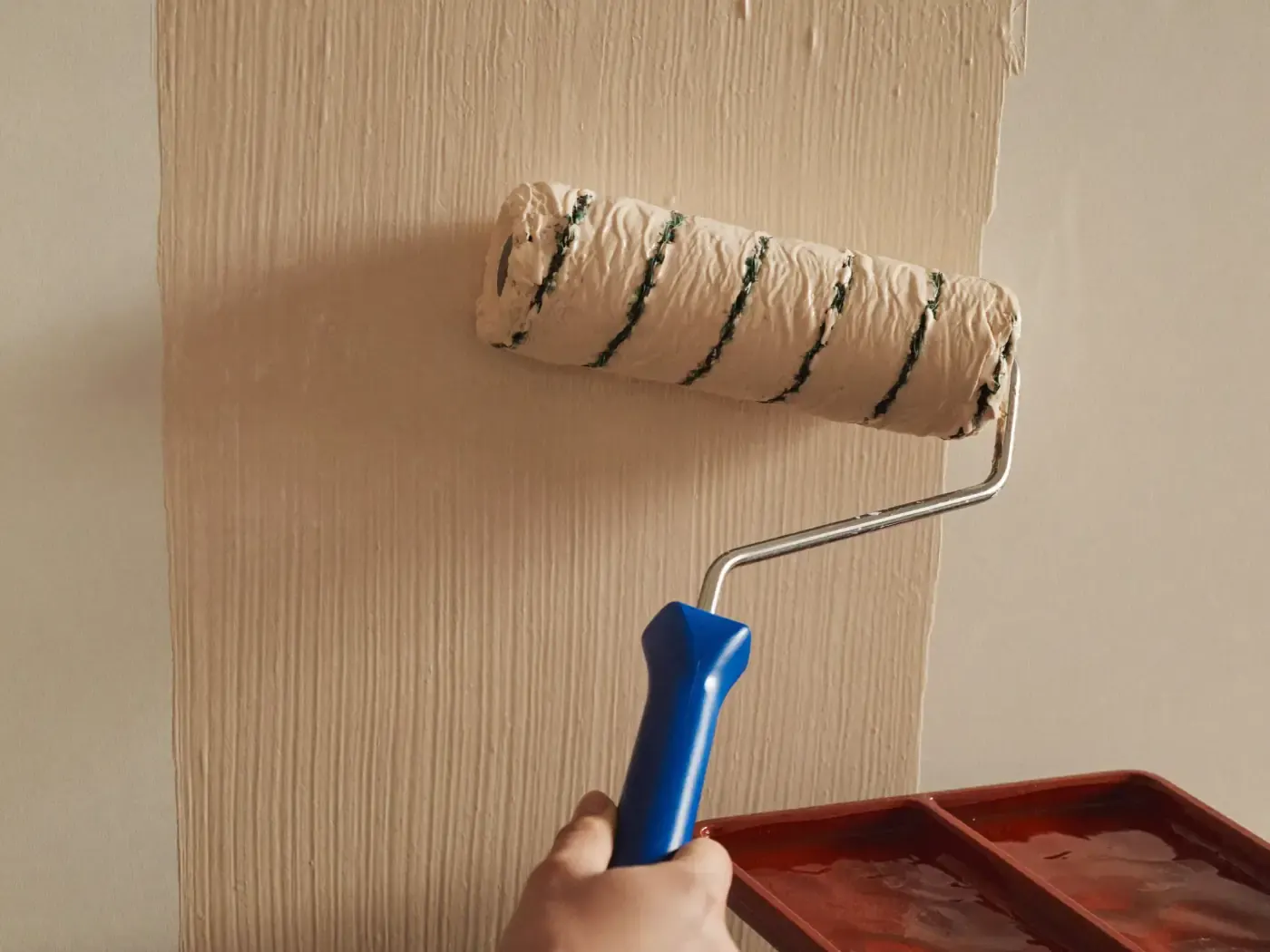 Rodillo aplicando pintura crema sobre pared lisa